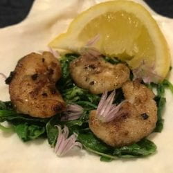 3 walleye cheeks on a bed of sauteed greens with a lemon wedge