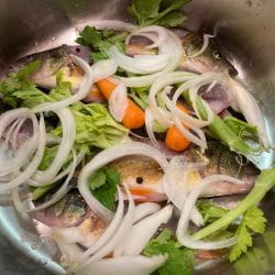 vegetables place on top of perch fish in stock pot