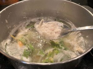 skimming foam with a slotted spoon from the fish stock cooking in a stock pot