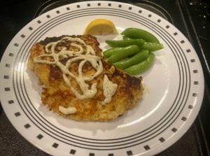 2 fish patties on a plate with a lemon wedge, snow peas, and a drizzle of aioli sauce
