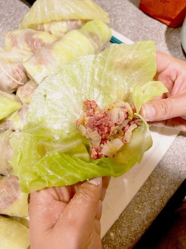 adding the meat stuffing mixture to the cabbage leaf and preparing to roll it up