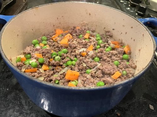 browned meat, with onion, carrot, and peas in Dutch oven